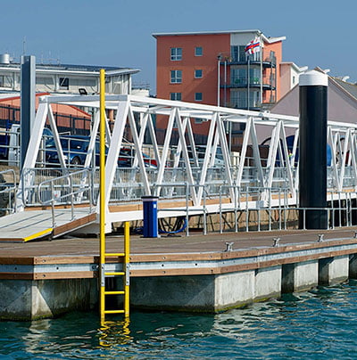 Gelbe Walcon -Sicherheitsleiter mit Grippost, montiert auf einem Gerüst in einem Hafen, um einen sicheren Zugang zum Wasser zu erhalten.