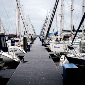 Een levendig uitzicht op een jachthaven vol met zeilboten, langs een strak, donkergrijs loopdek, gemaakt van antracietkleurige Geveka-dekdelen.