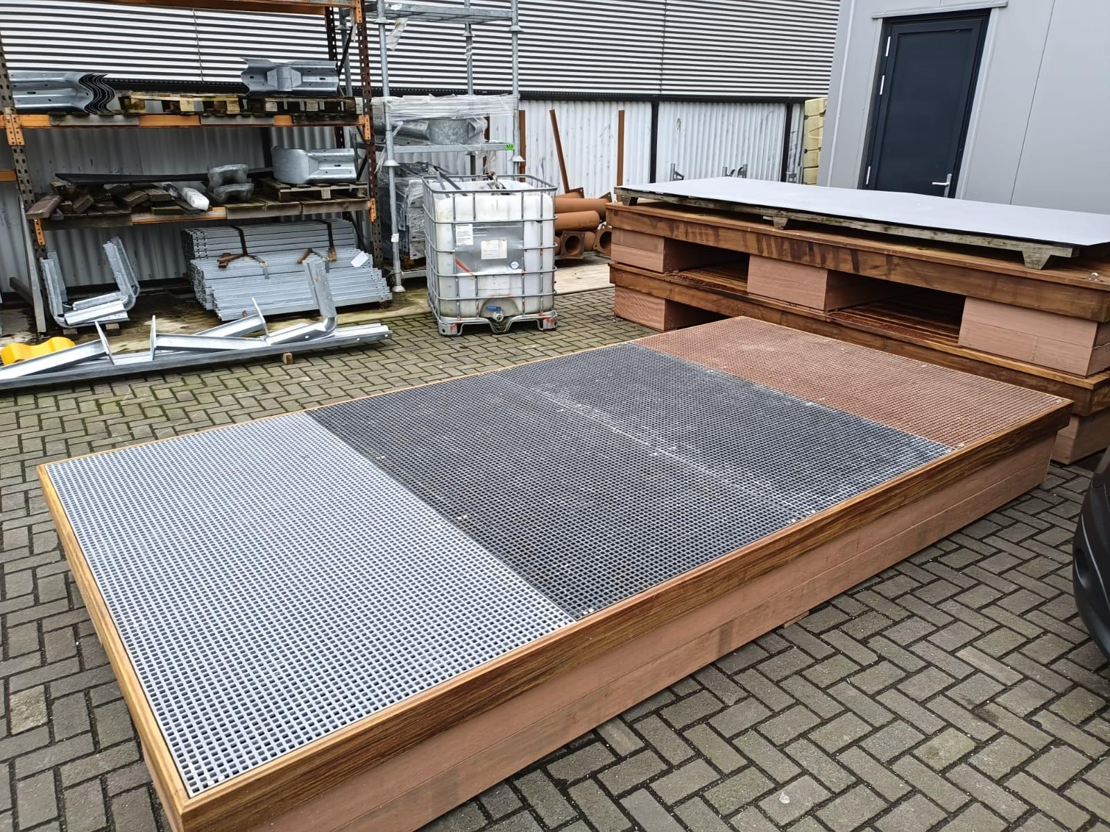 Een drijvend terras in productie met een GVK-roosterdek en houten afwerking. Het terras is zichtbaar in een werkplaatsomgeving met diverse bouwmaterialen en gereedschappen op de achtergrond. Het ontwerp combineert functionaliteit en duurzaamheid, ideaal voor maritieme toepassingen.