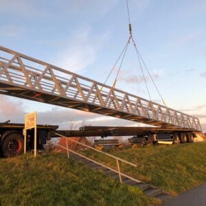 Ein Aluminiumweg wird von einem Kran über einem Lastwagen auf einem Rasen angehoben.