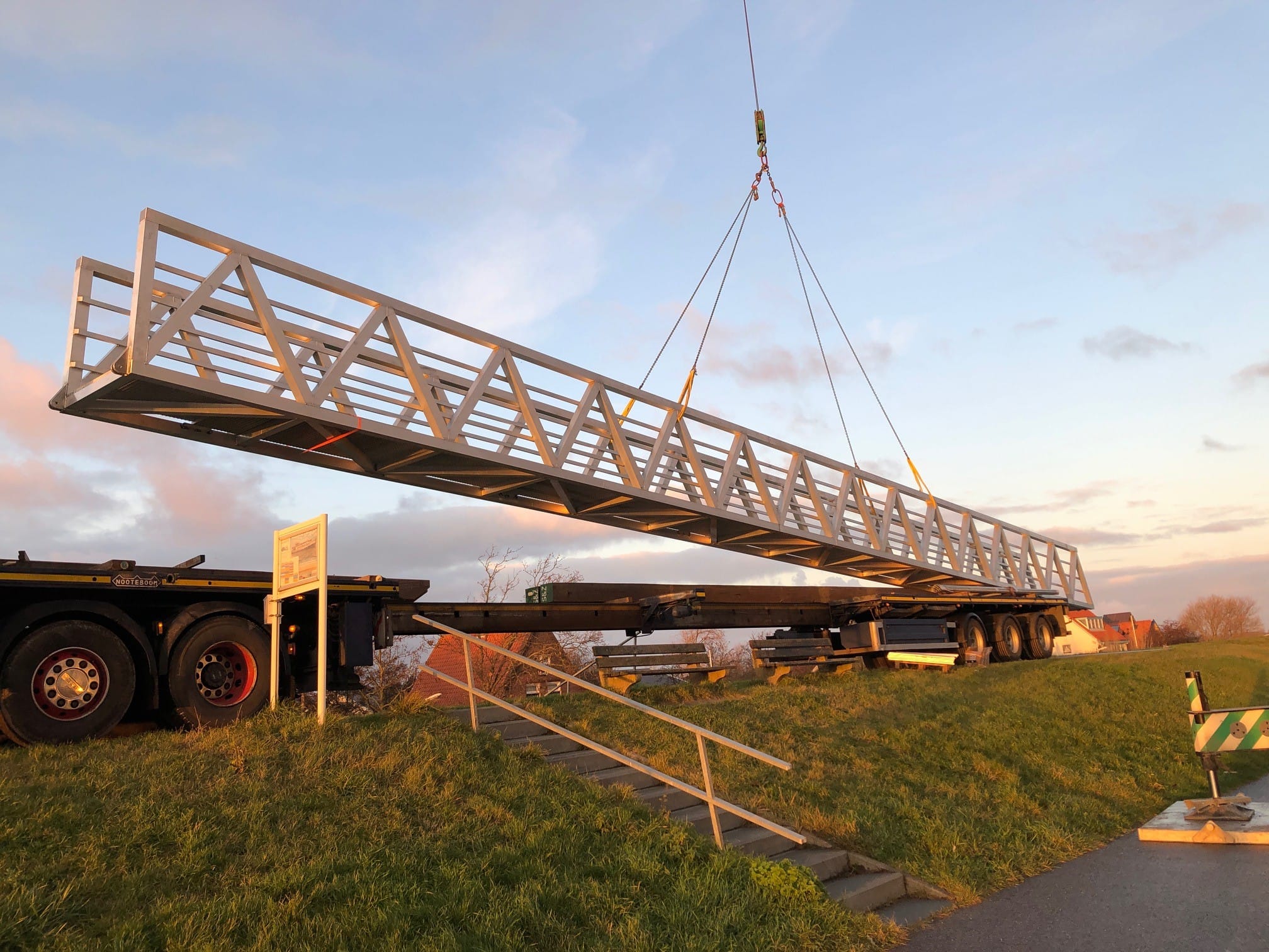 Ein Aluminiumweg wird von einem Kran über einem Lastwagen auf einem Rasen angehoben.