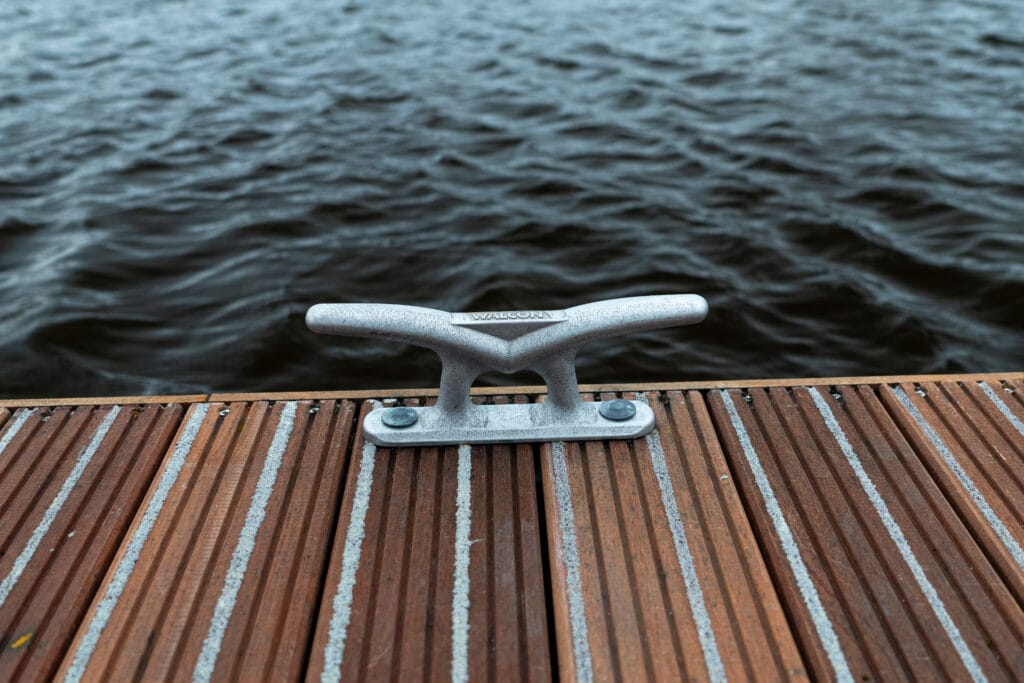 Een Walcon kikker stevig gemonteerd op een houten steiger met antislipstrips, tegen de achtergrond van een wateroppervlak met lichte golfslag. Ideaal voor het veilig vastmaken van touwen in een maritieme omgeving.