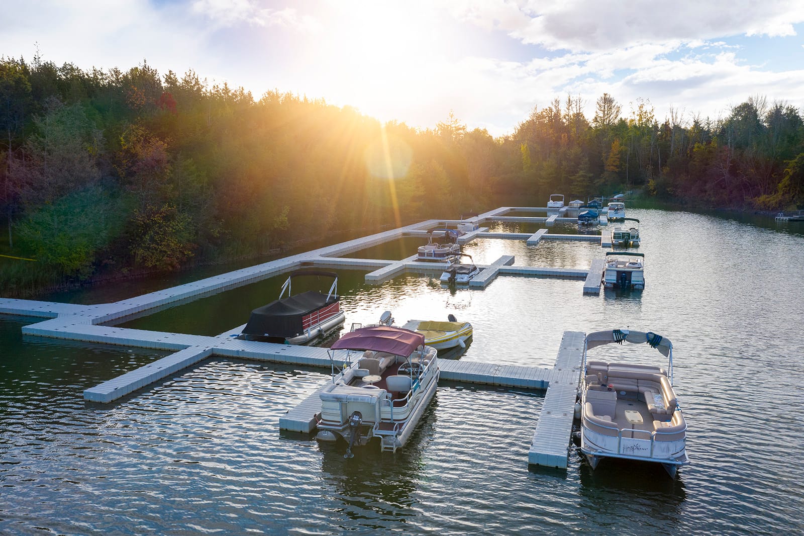  Drijvende EZ Dock steigers met aangemeerde boten op een rustig meer, omringd door bomen en zonlicht.