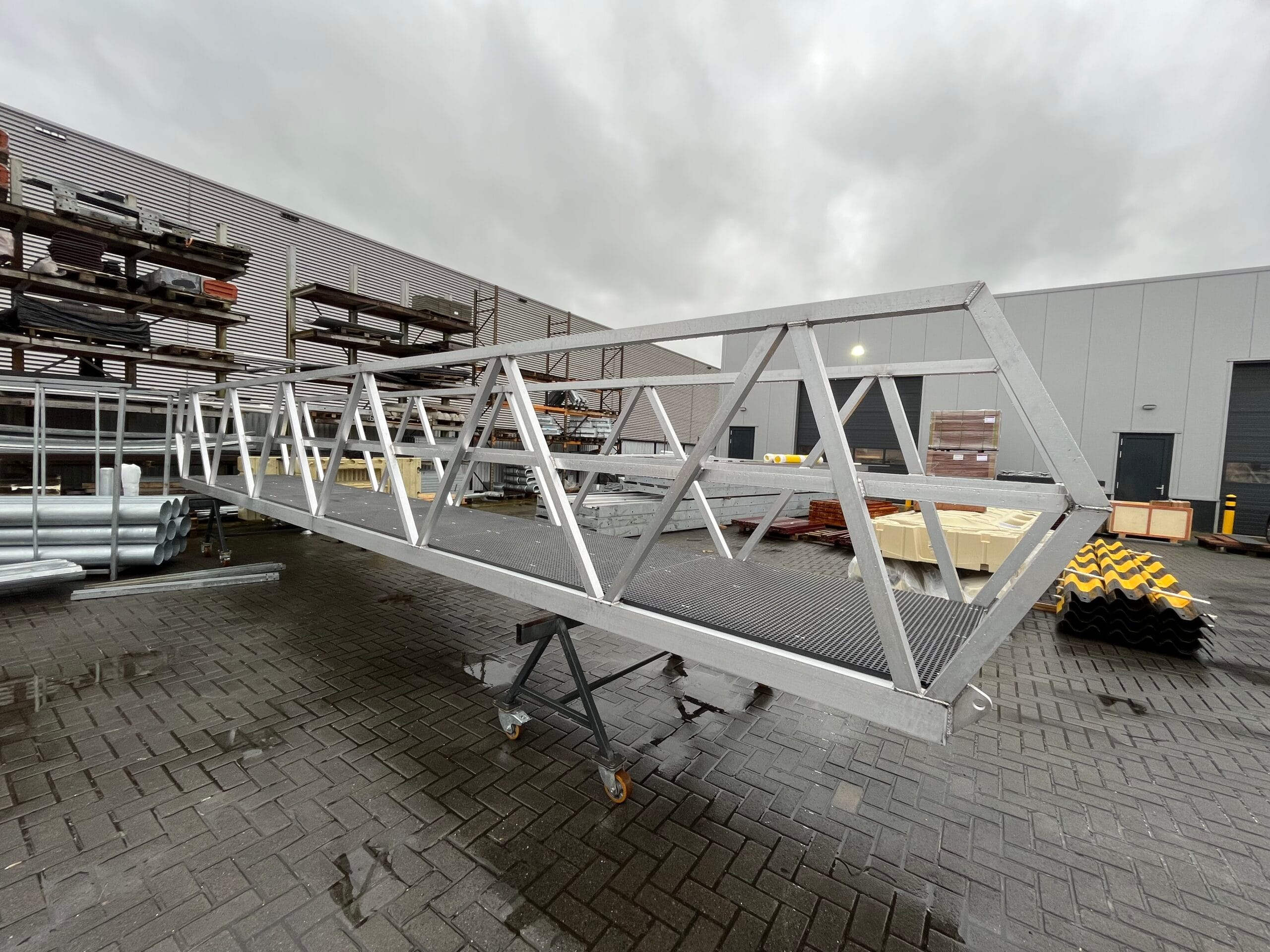 Aluminum walkway with a triangular structure, placed on a chassis in an industrial environment.