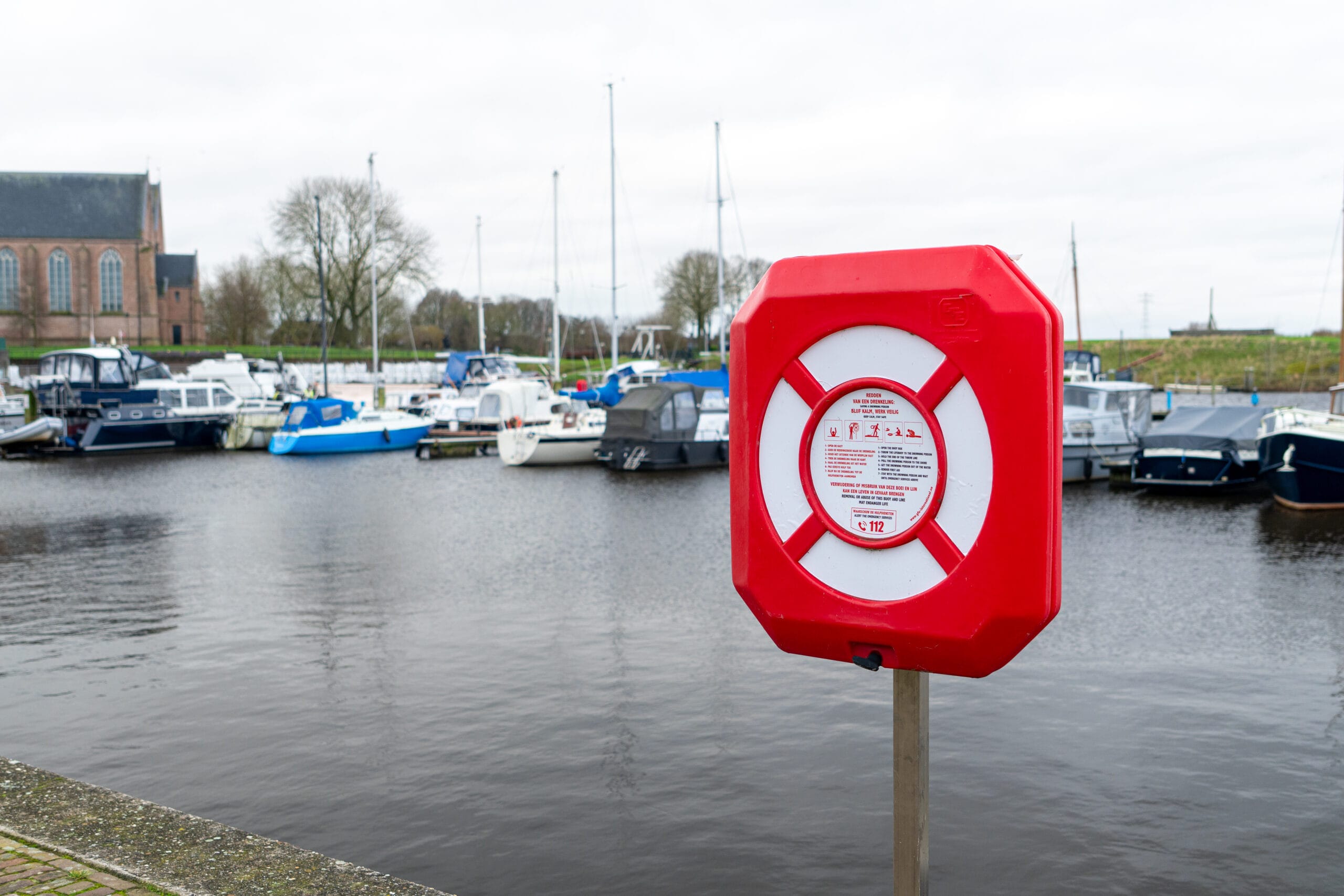 Reddingsboeikast geplaatst op een kade, inclusief reddingsboei, geschikt voor havenveiligheid.
